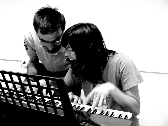 two adults playing a piano keyboard and laughing