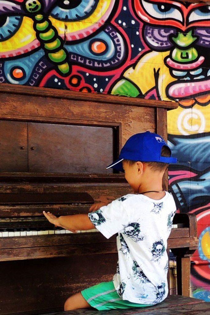 a young boy playing piano against a colourful wall