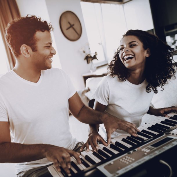 two adults smiling while playing a piano duet