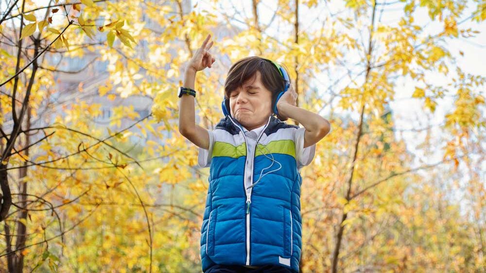 young boy listening to music on headphones throwing up his hand