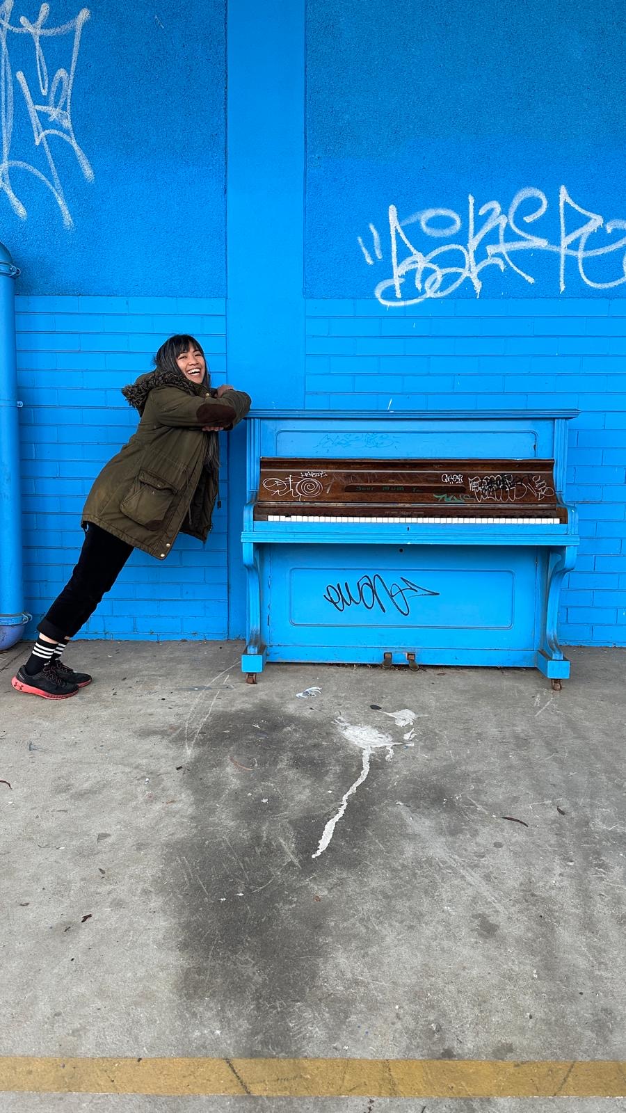 A piano teacher smiling and leaning on a vintage blue acoustic piano